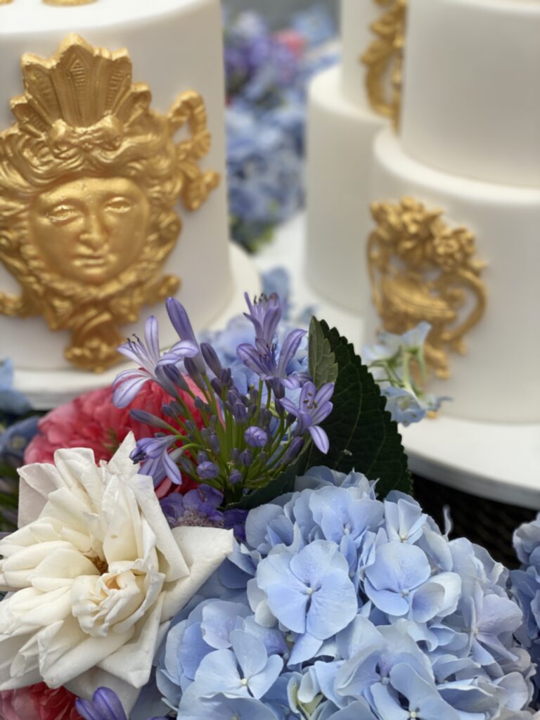 Gold and white cake with hydrangeas, roses and agapanthus flowers.
